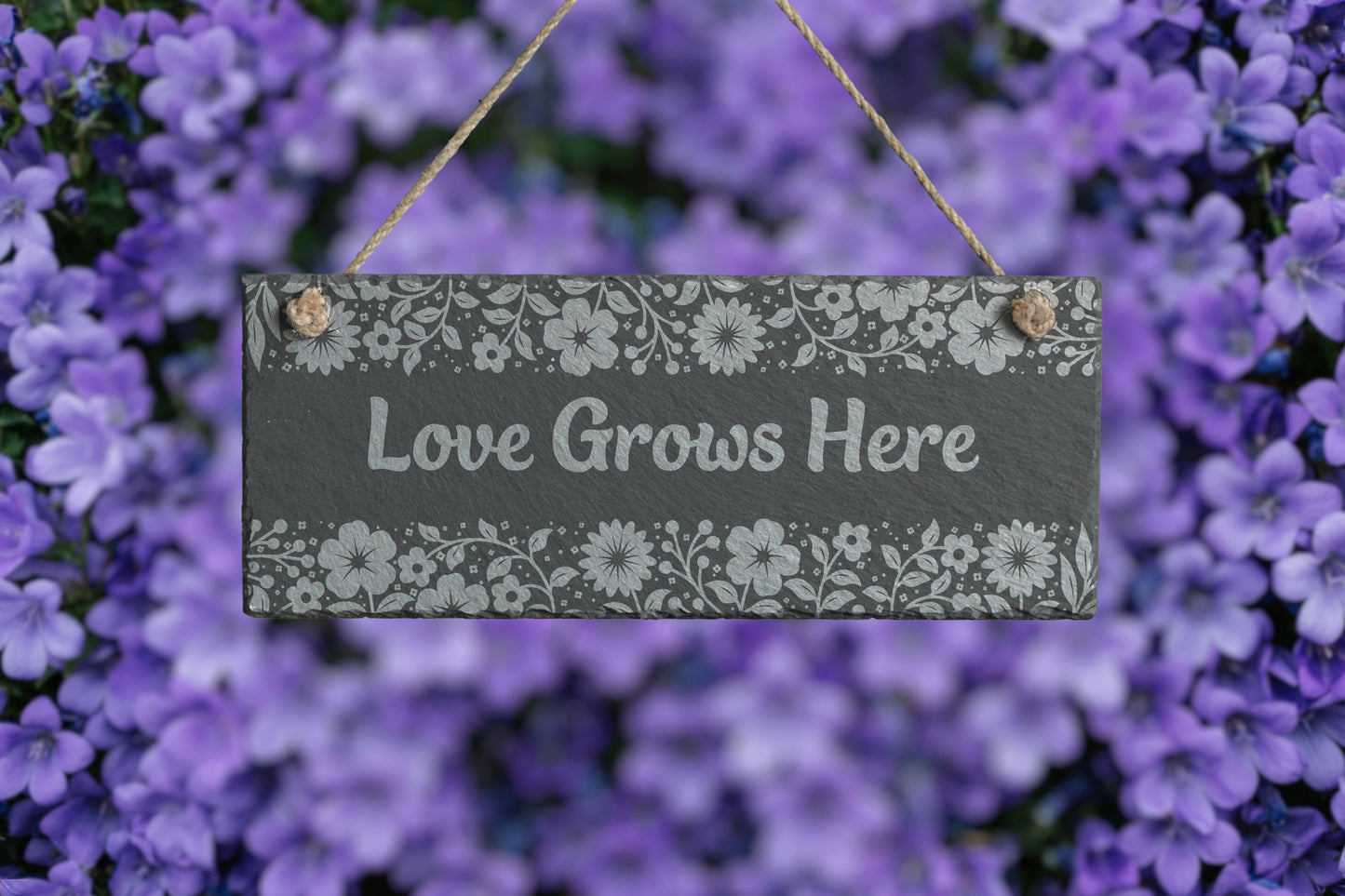 Customizable slate sign with engraved floral border and the text 'Love Grows Here', hanging in a garden setting.