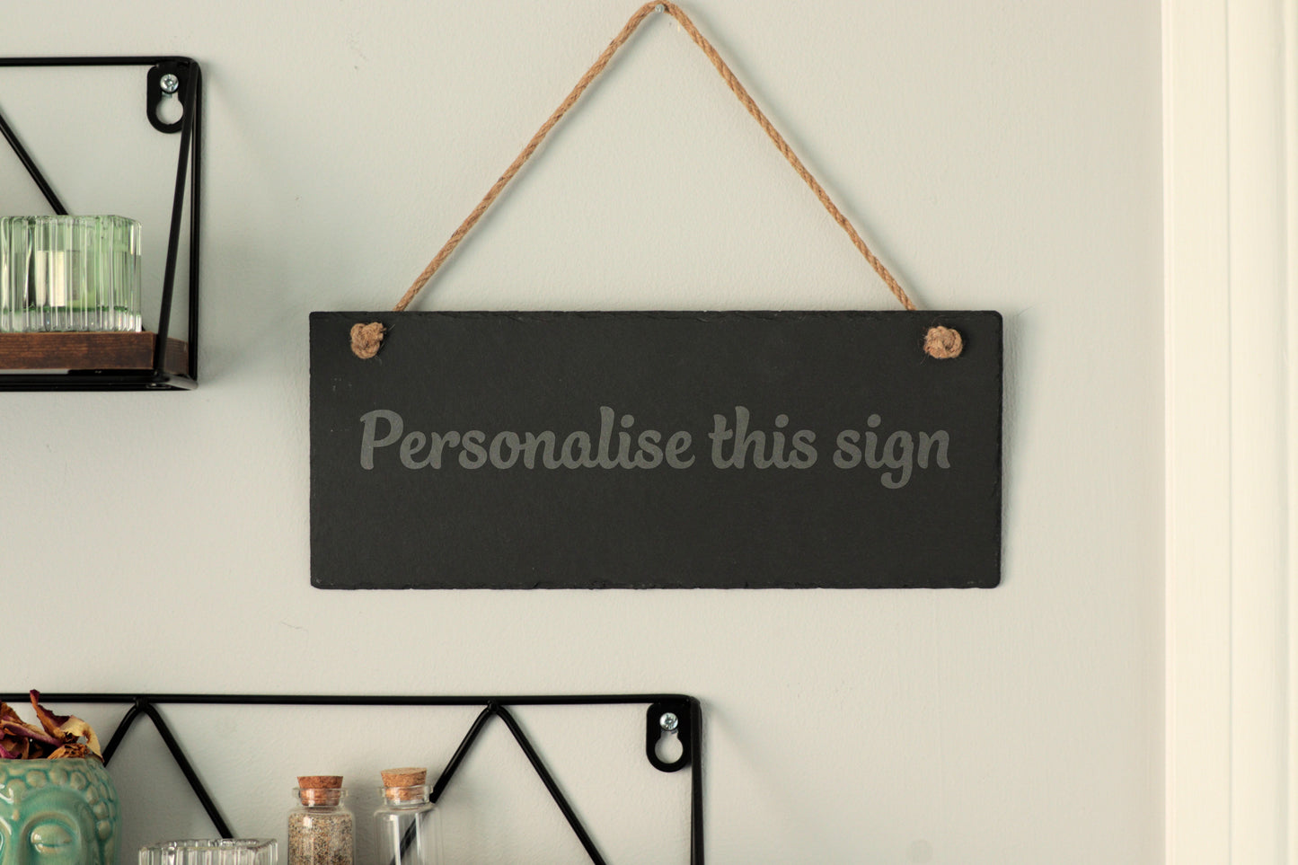 Customizable slate sign with the text 'Personalise this sign', hanging on a wall near shelves.