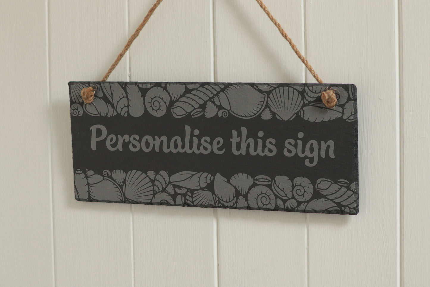 Customizable engraved slate sign with sea shell border, hanging on rope, with the text 'Grow with the Flow', displayed against a white wooden background.