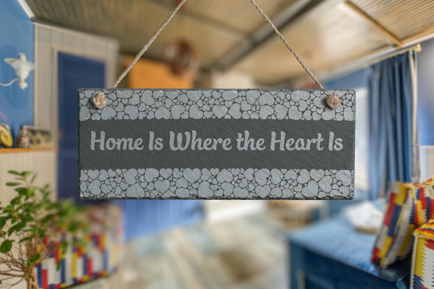 Customizable slate sign with engraved heart border and the text 'Home is Where the Heart Is', hanging in a living room setting.