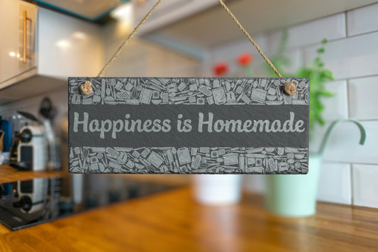 Customizable slate sign with engraved kitchen utensil border and the text 'Happiness is Homemade', hanging in a modern kitchen setting.