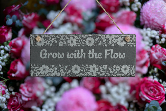 Customizable slate sign with engraved floral border and the text 'Grow with the Flow', hanging in a garden setting.