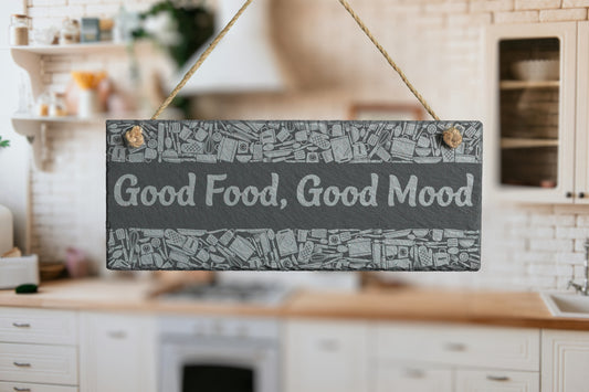 Customizable slate sign with engraved kitchen utensil border and the text 'Good Food, Good Mood', hanging in a modern kitchen setting.