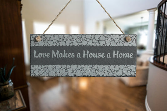 Customizable slate sign with engraved heart border and the text 'Love Makes a House a Home', hanging in a living room setting.