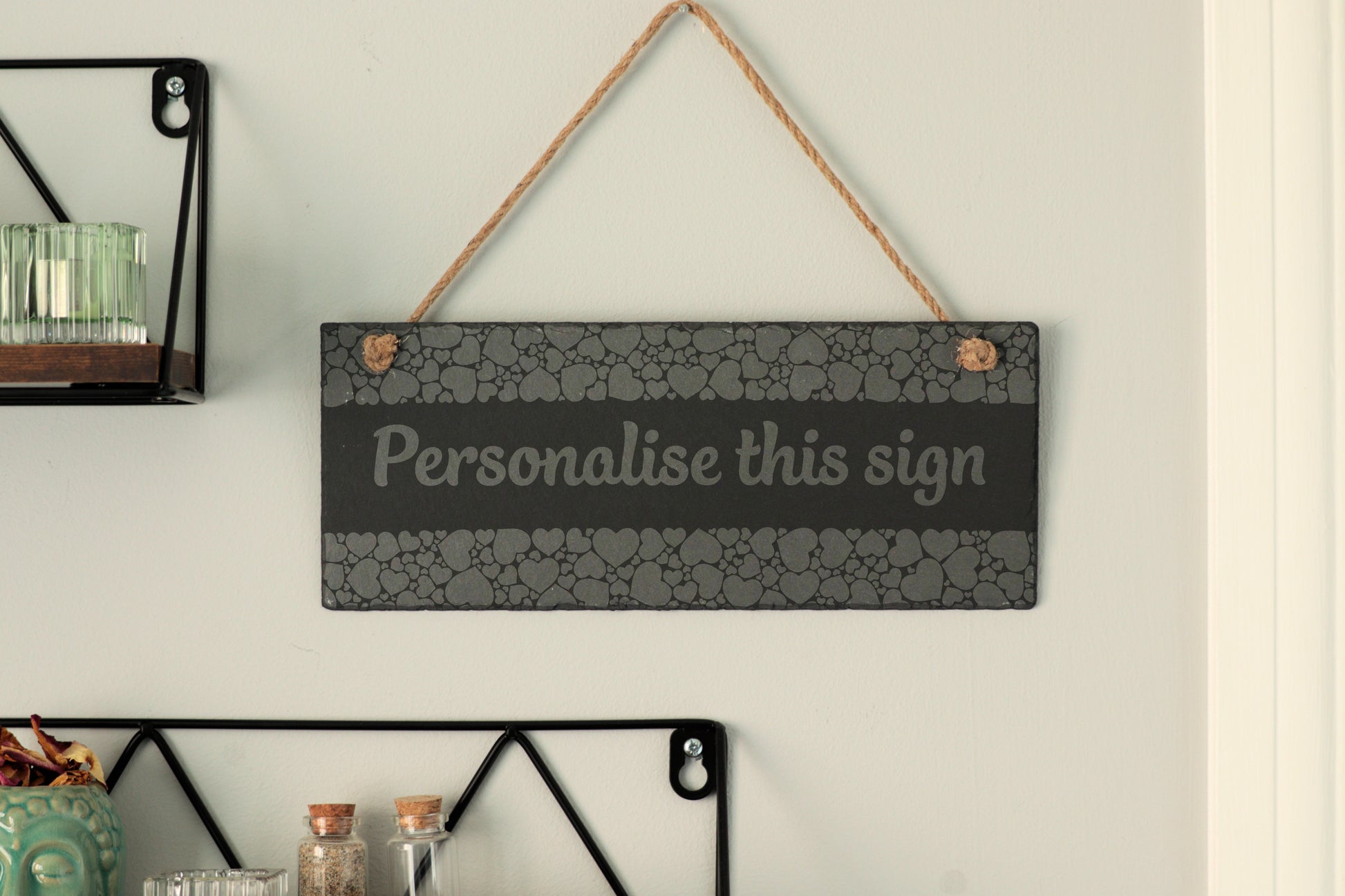 Customizable slate sign with heart border and the text 'Personalise this sign', hanging on a wall near shelves.