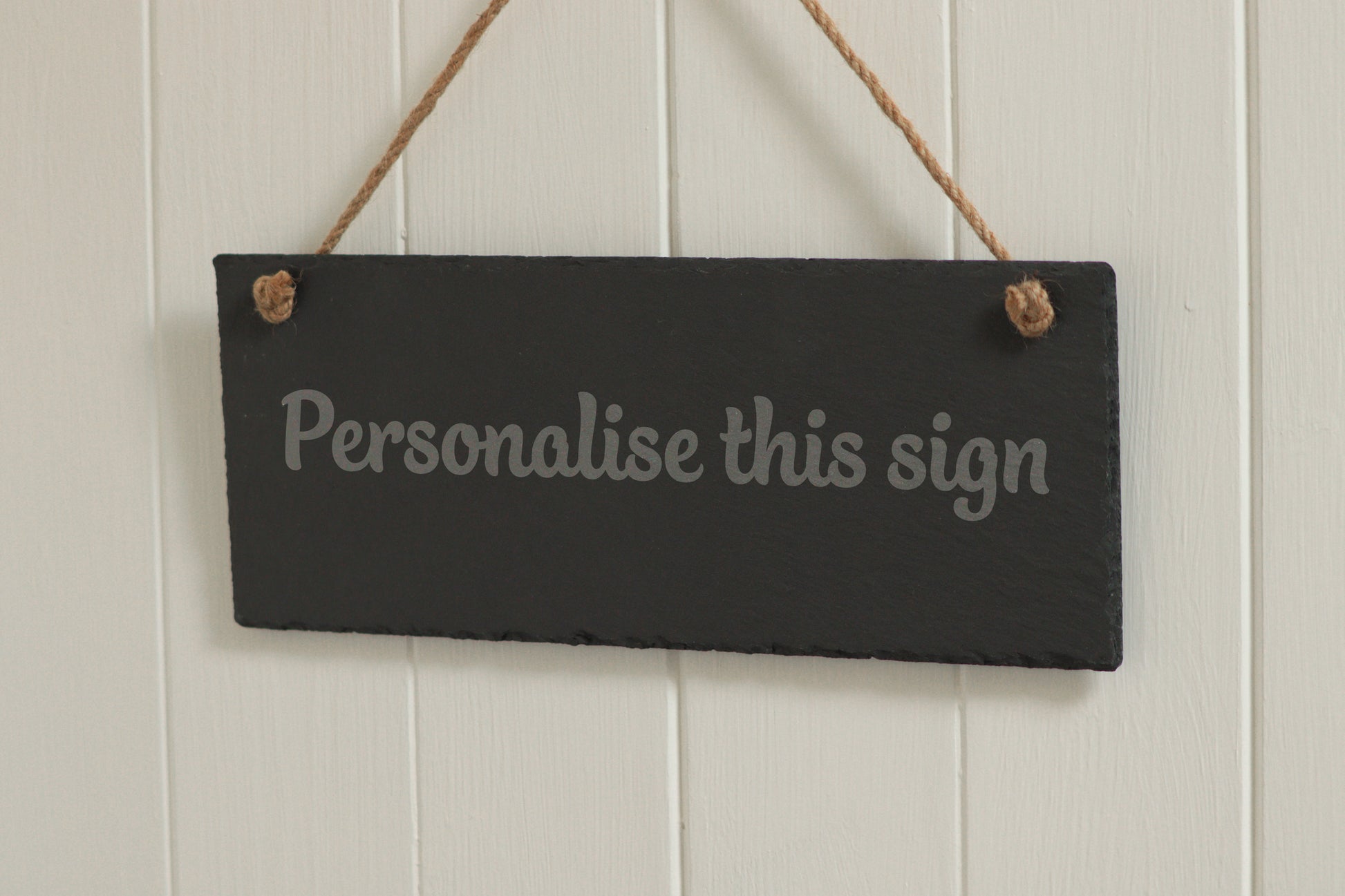 Customizable engraved slate sign, hanging on rope, with the text 'Personalise this sign', displayed against a white wooden background.